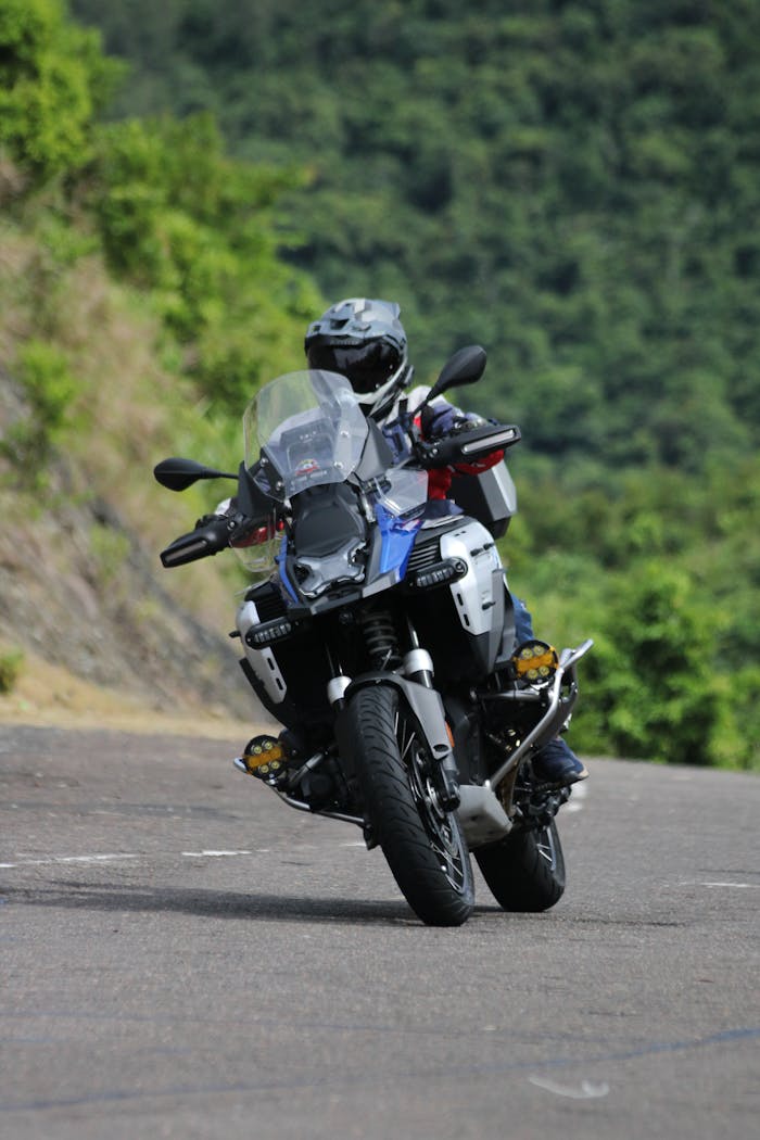 A motorcyclist navigates a winding mountain road surrounded by lush greenery, showcasing adventure.